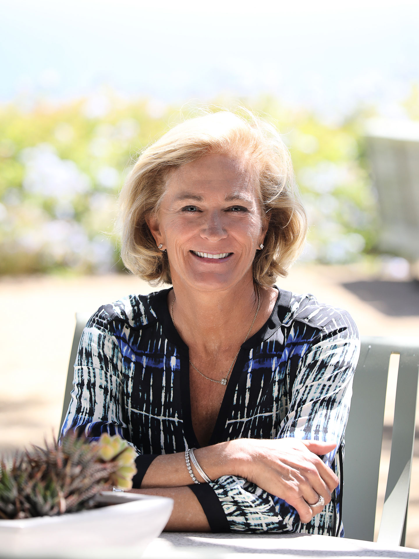 Portrait of Gretchen Burke in a blue, black, and white patterned dress sitting outside at a table