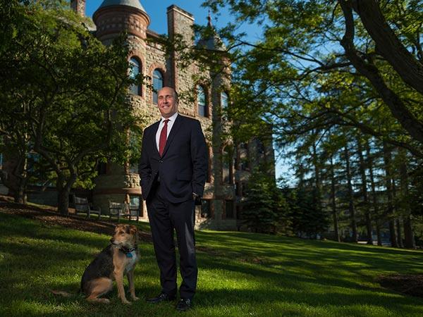 President Casey poses for a portrait on campus, standing next to his loyal dog Emrys