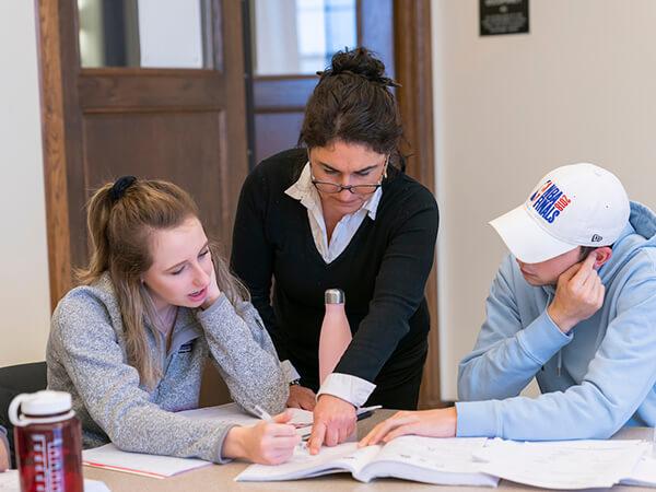 Professor Anat Guez points to a note on a page while working with two Colgate students in class