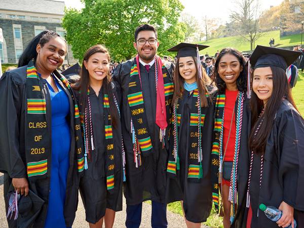 A group of students smile and pose for a photo in commencement gowns and hats.