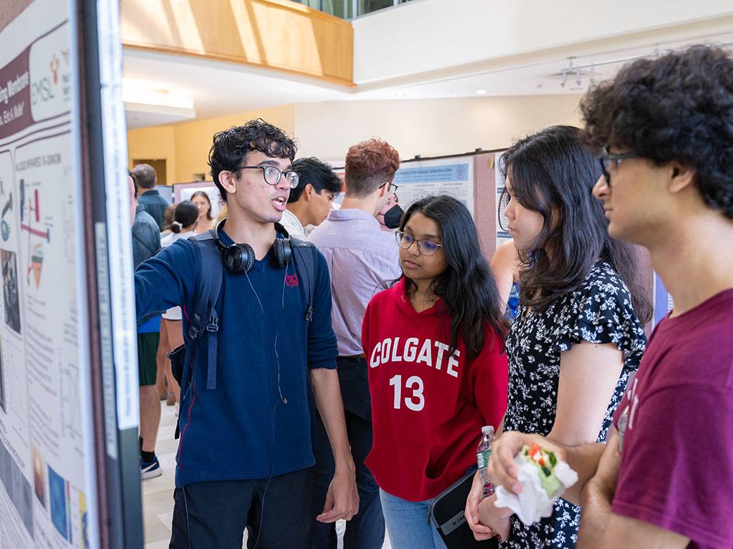 Three students gather around poster presentation