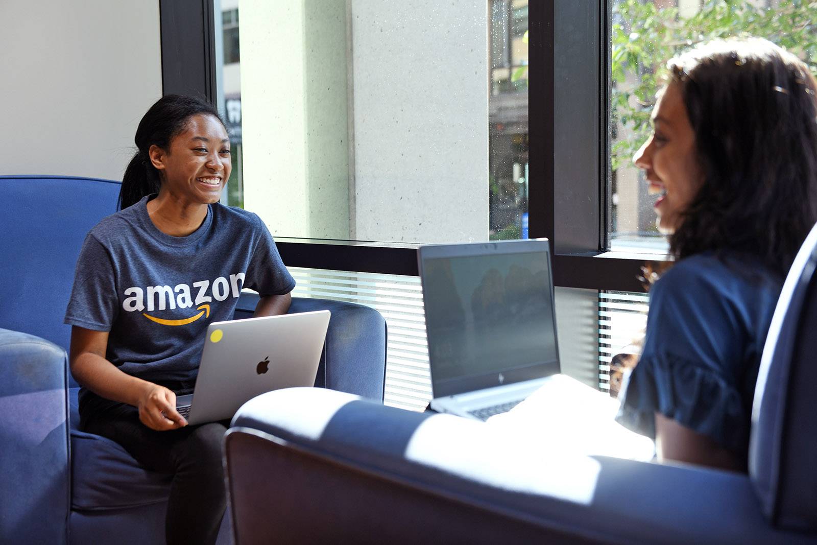 Two people with lap tops sit in chairs facing each other