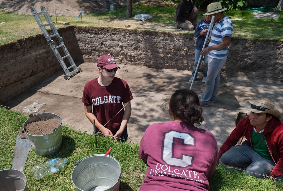 Three students wearing Colgate t-shirts at an excavation site in Mexico