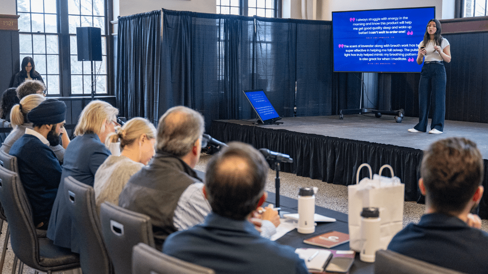 A student pitches her venture on stage while seated judges look on