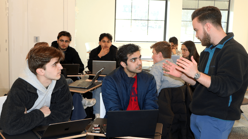EIR Reece Wilson animatedly talking with two students seated at their laptops