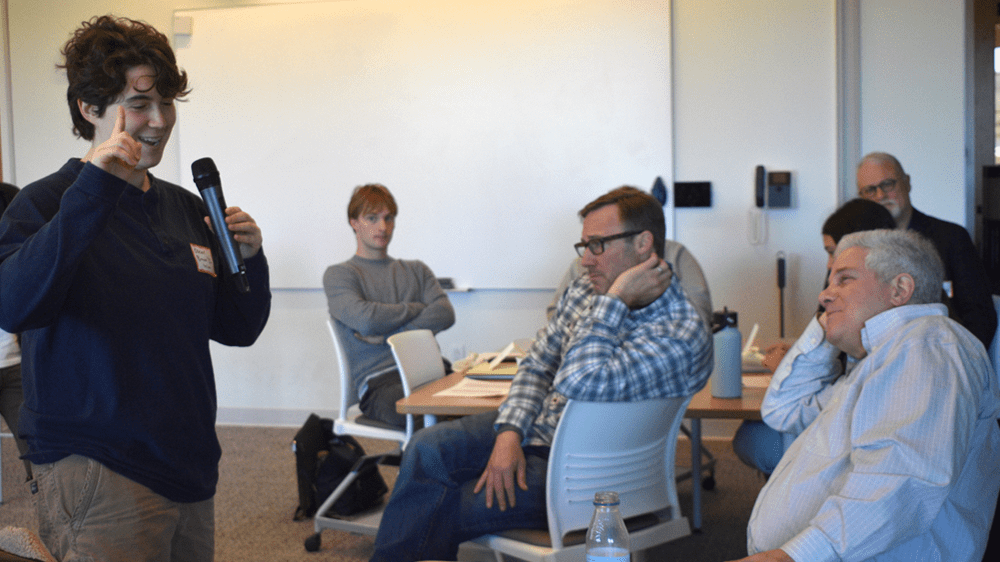 Oscar Brown standing and holding his finger to his head, sharing his idea to a classroom of seated alumni mentors.