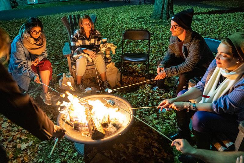 Students gather around a fire pit roasting marshmallows