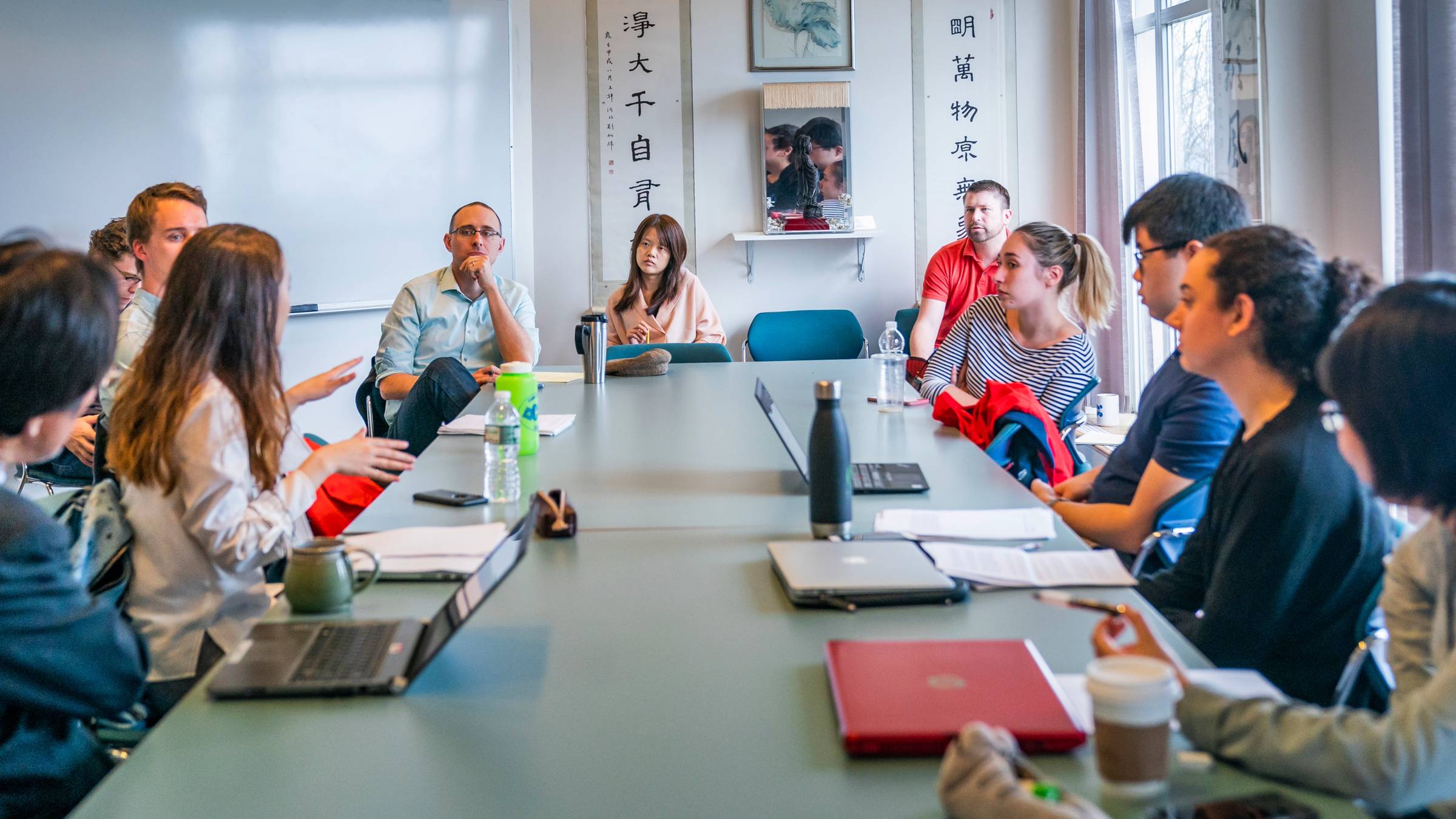 Economics students share presentations with professor while gathered around table