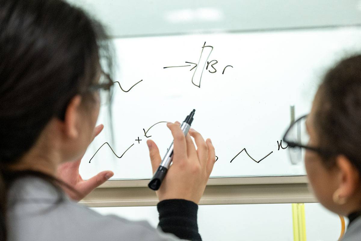 Two women at a glass board solving an equation