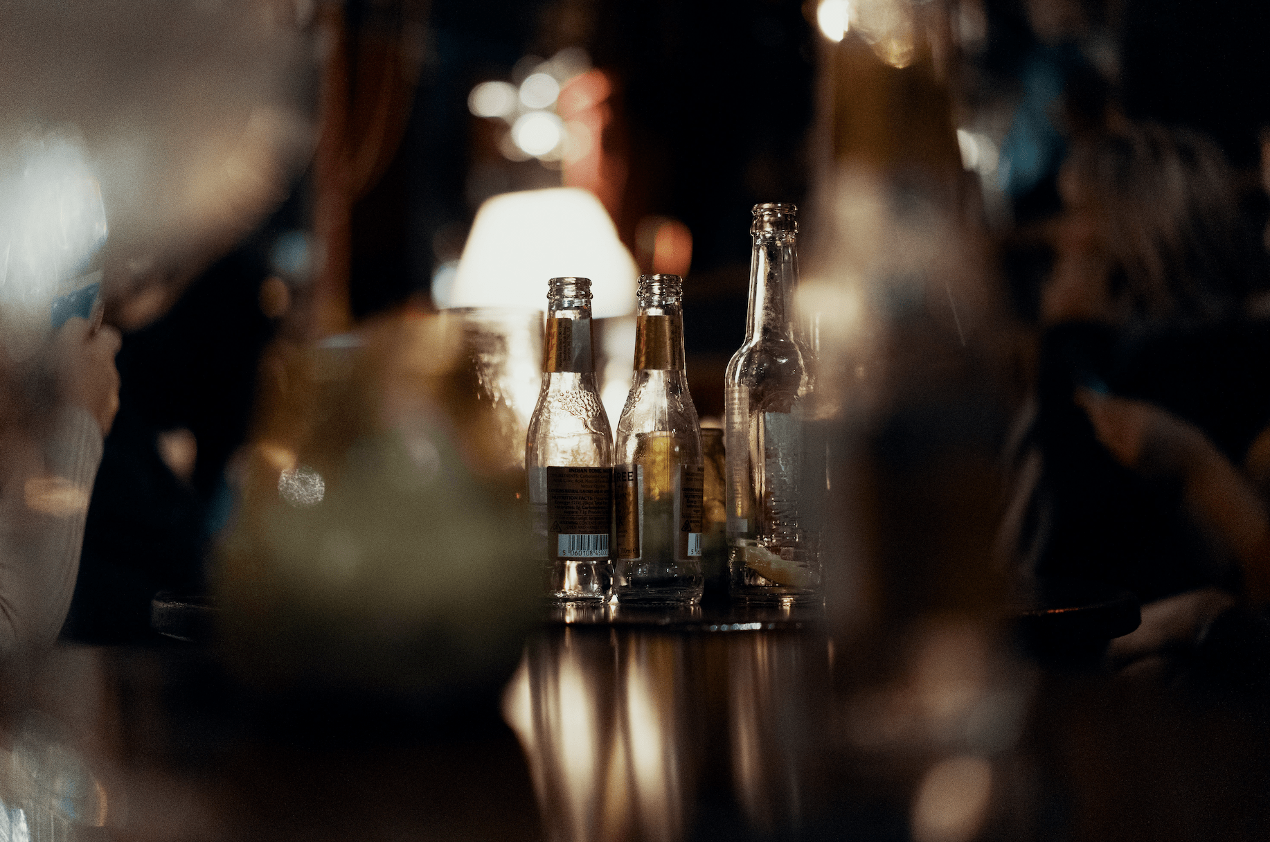 Empty beer bottles sit on a dimly-lit table.