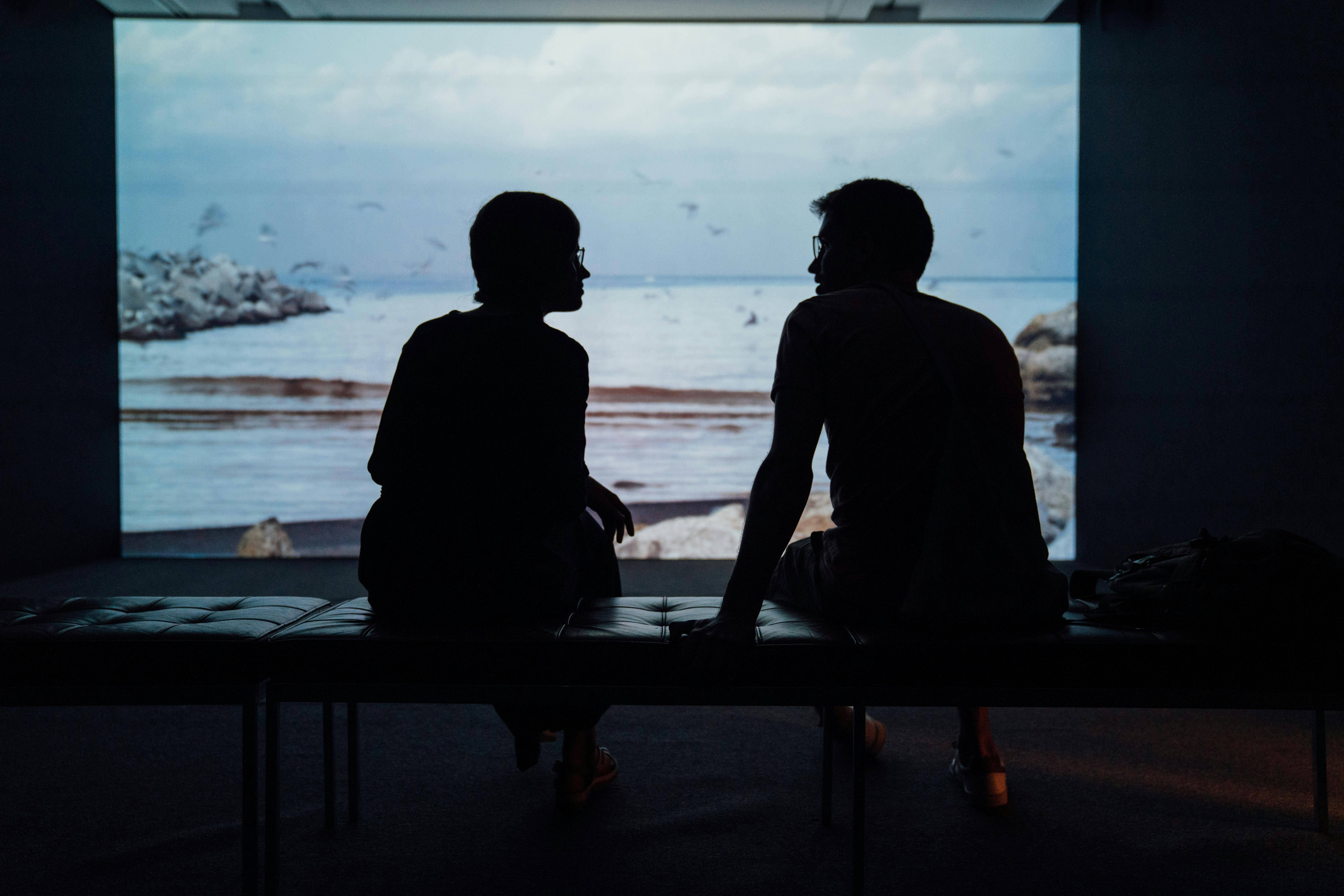 Silhouettes of a man and woman sitting on a bench.