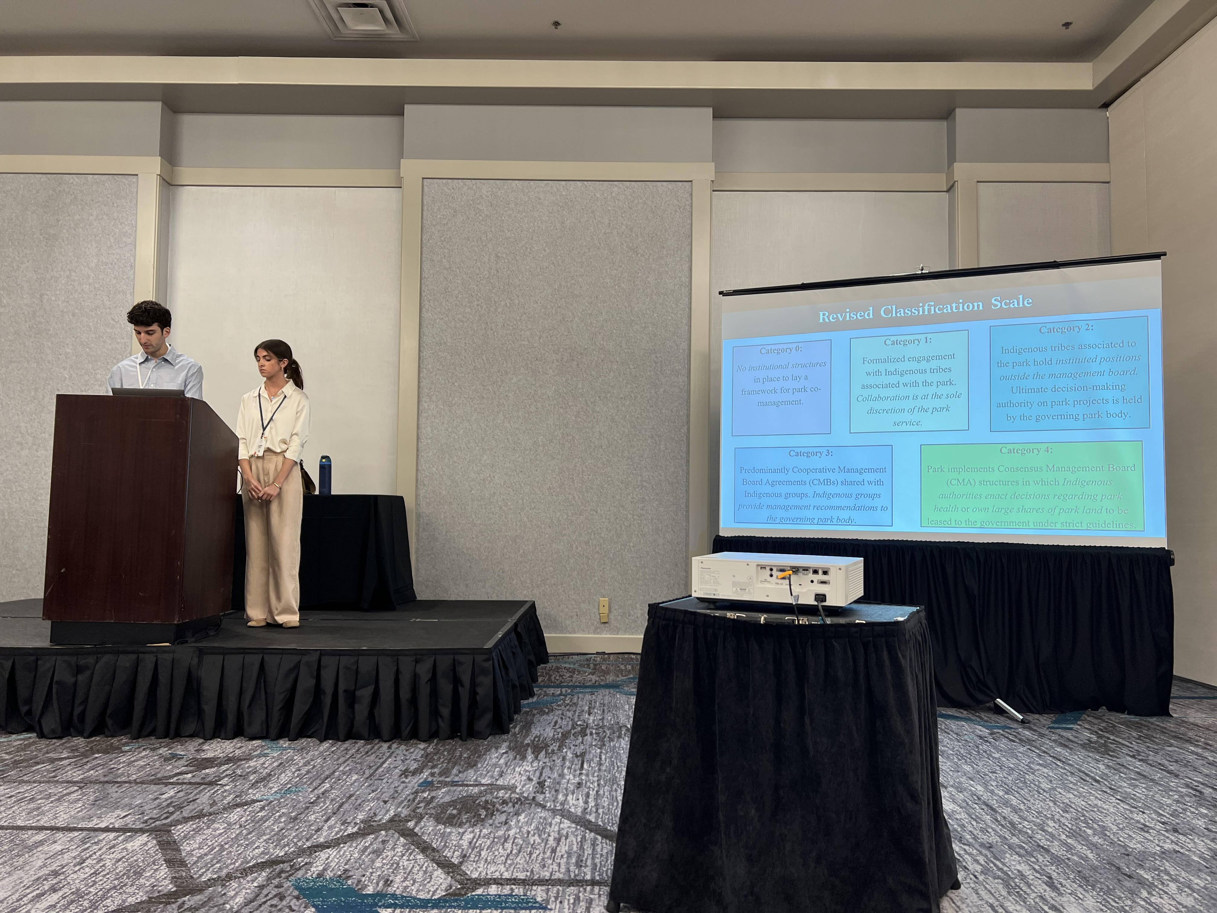 Students presenting at a podium with a screen on their right.